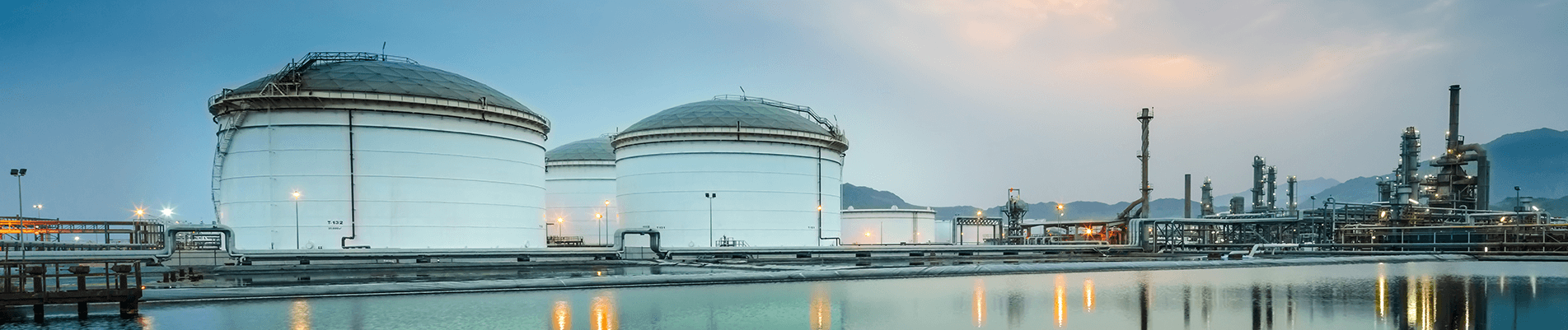 Terminal tanks and refinery at dusk with mountains on the horizon