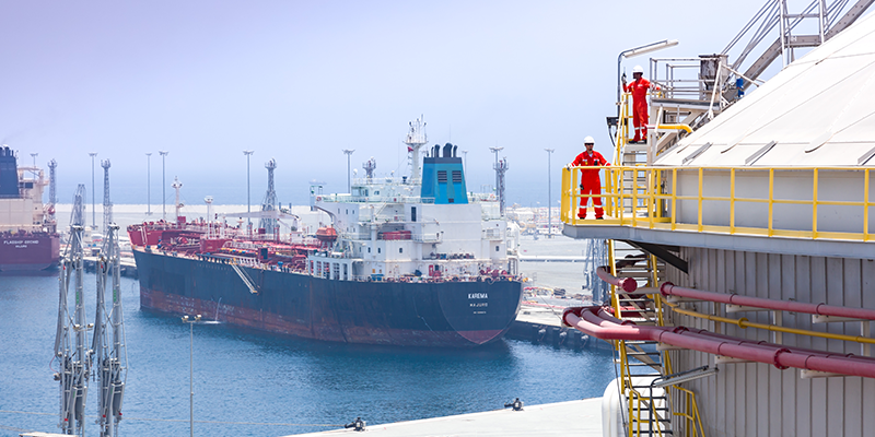 Engineers on the roof of a storage terminal with vessels loading at the jetty in the background